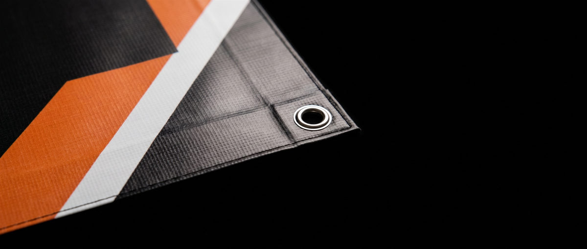 Close-up of a vinyl banner corner showing the scrim texture, full-color print, a heat-welded hem and a silver metal grommet